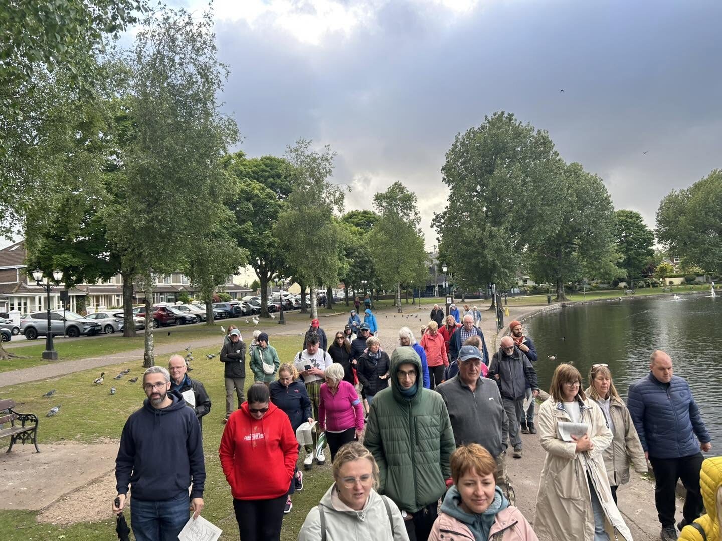 People of different ages walking along a path beside a pond lined with trees